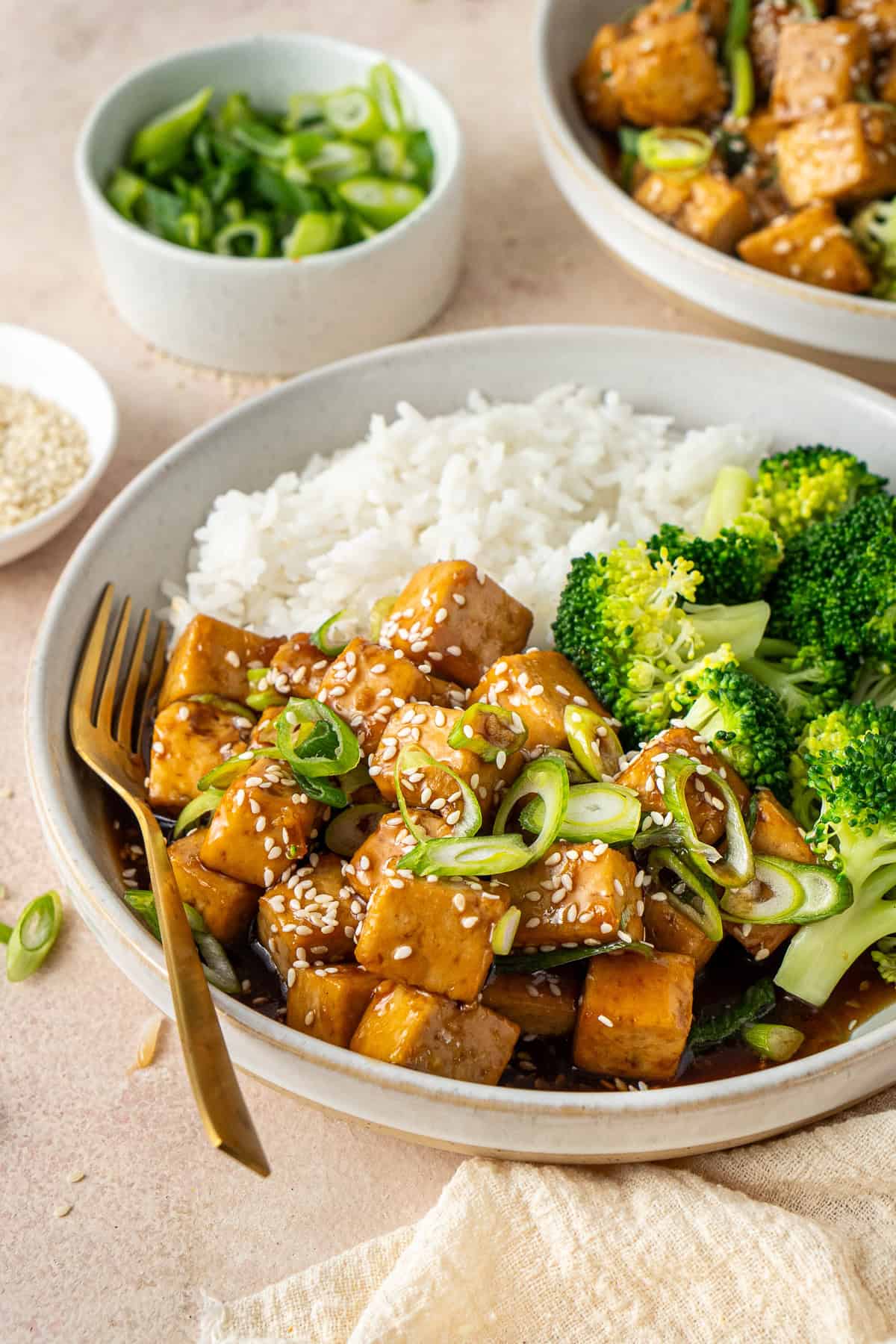 A fork in a bowl of teriyaki tofu, rice and broccoli.