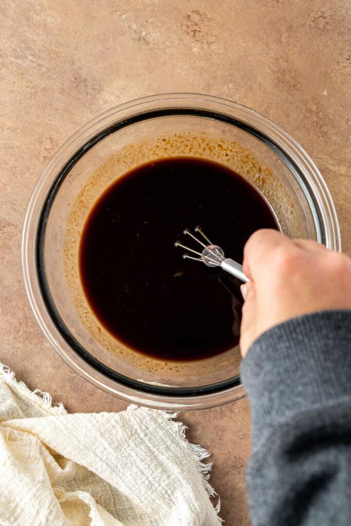 A hand whisking together the sauce in a small bowl.