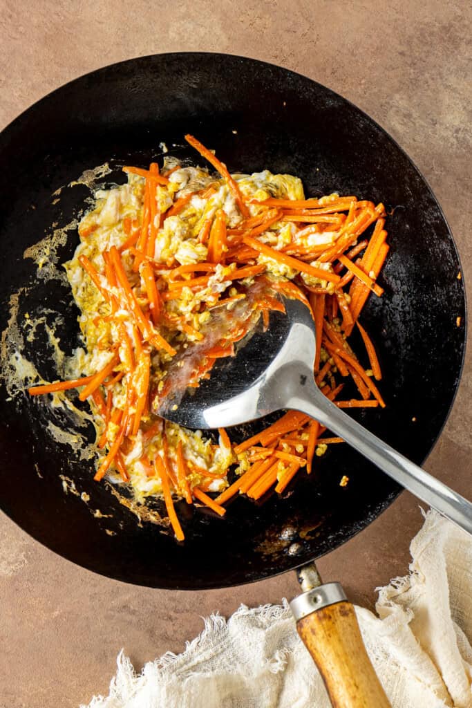 Stir-frying the carrots and egg in a wok.