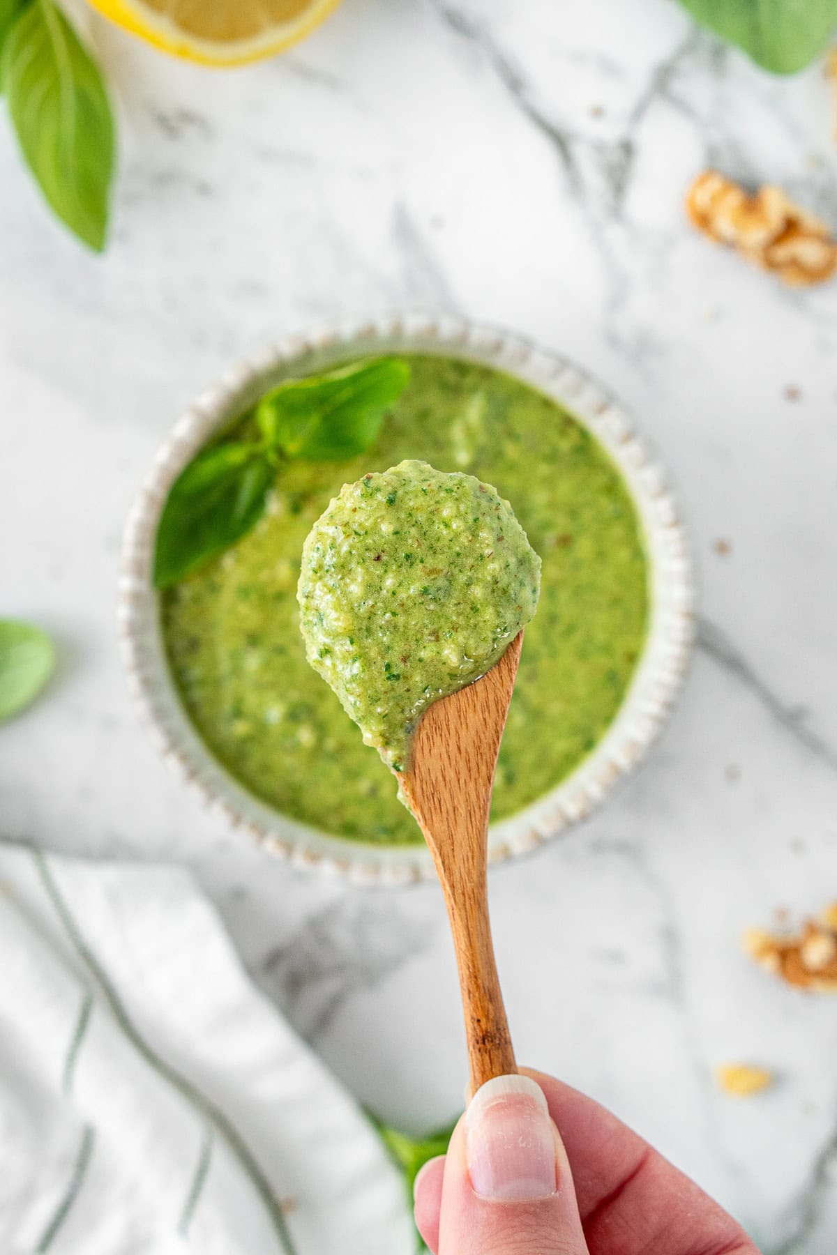 A hand holding a wooden spoon of basil pesto.