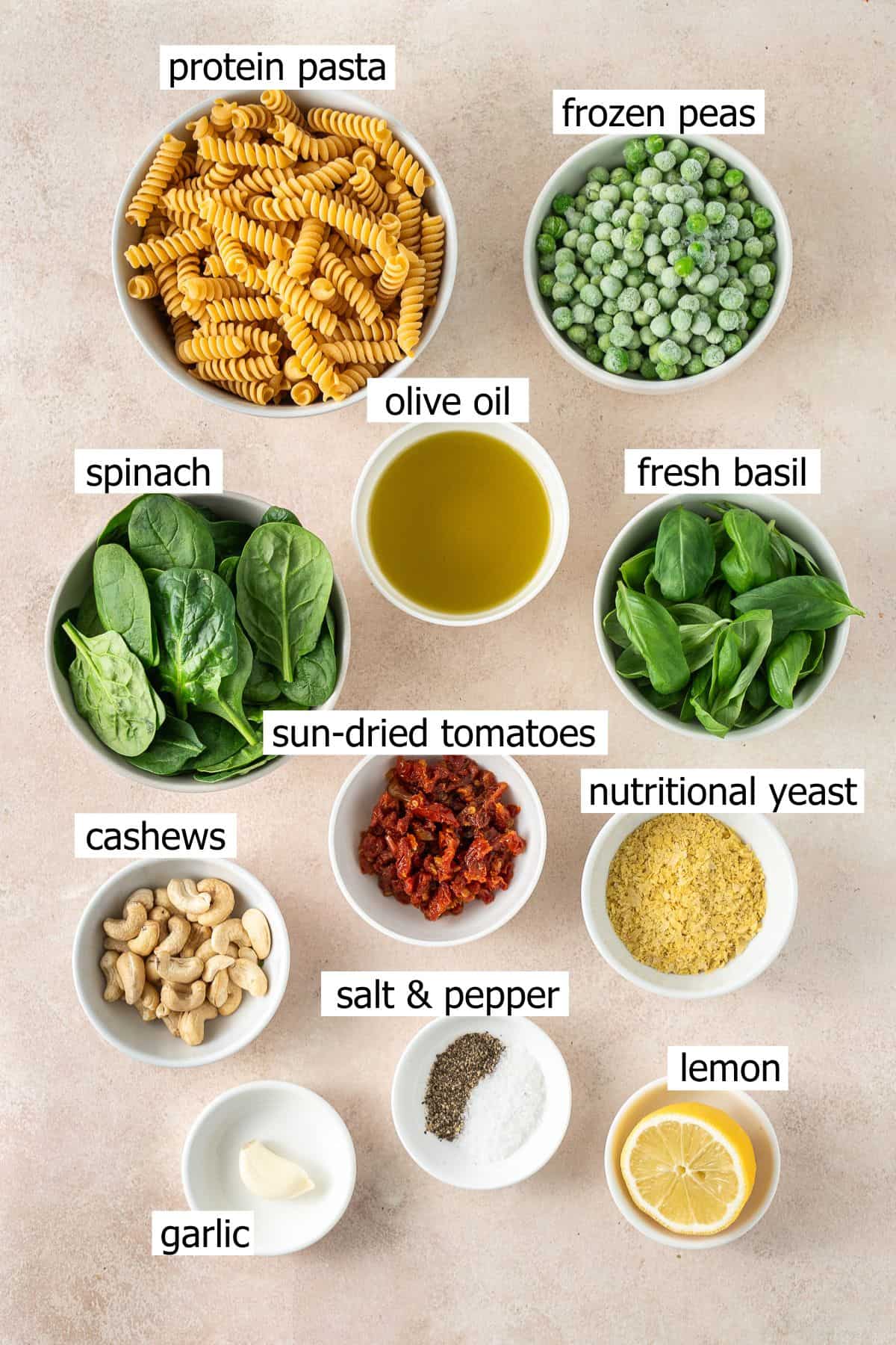 All ingredients needed to make high protein pea pesto pasta laid out in bowls.