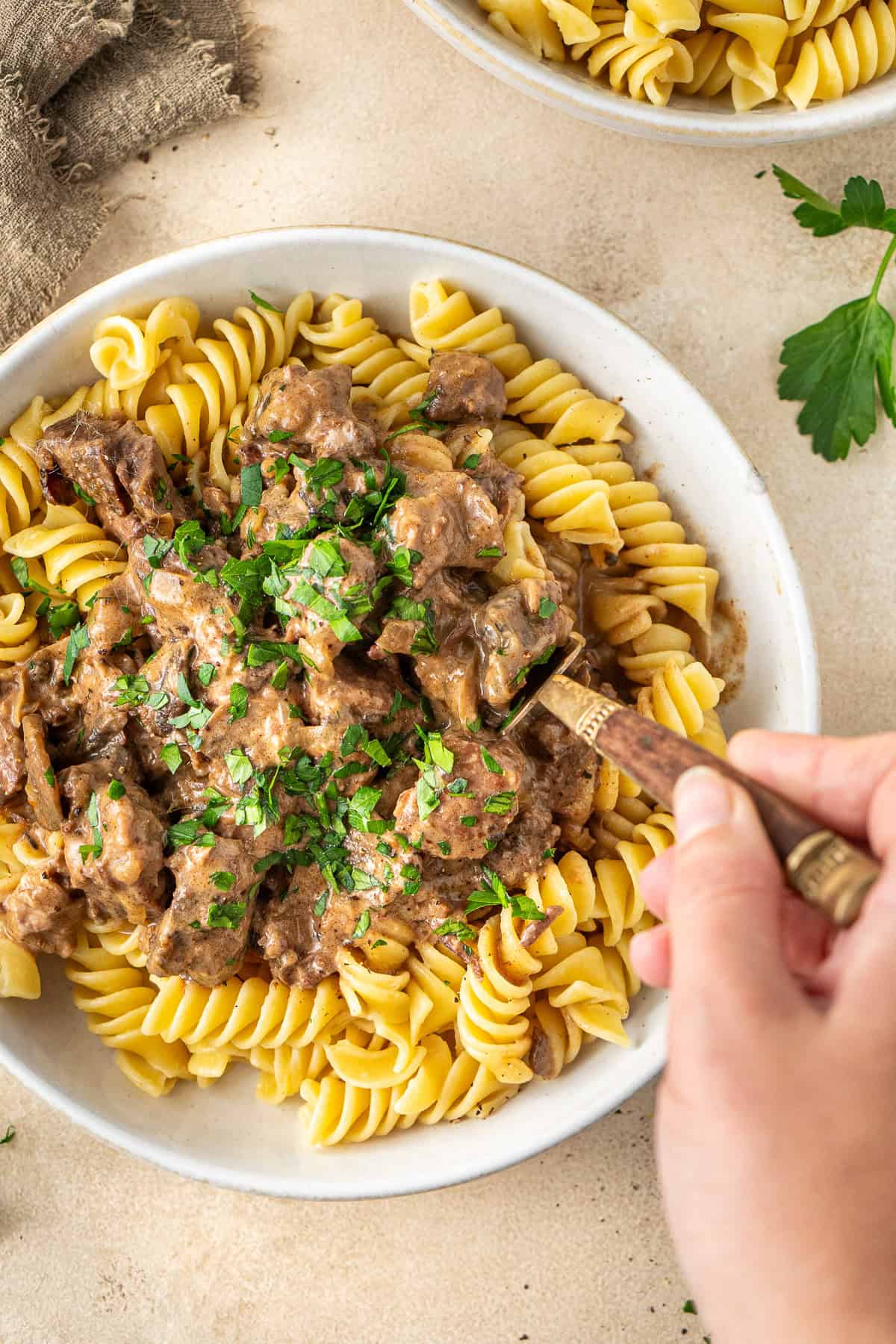 Close up of a handing holding a fork taking a bite of beef stroganoff.