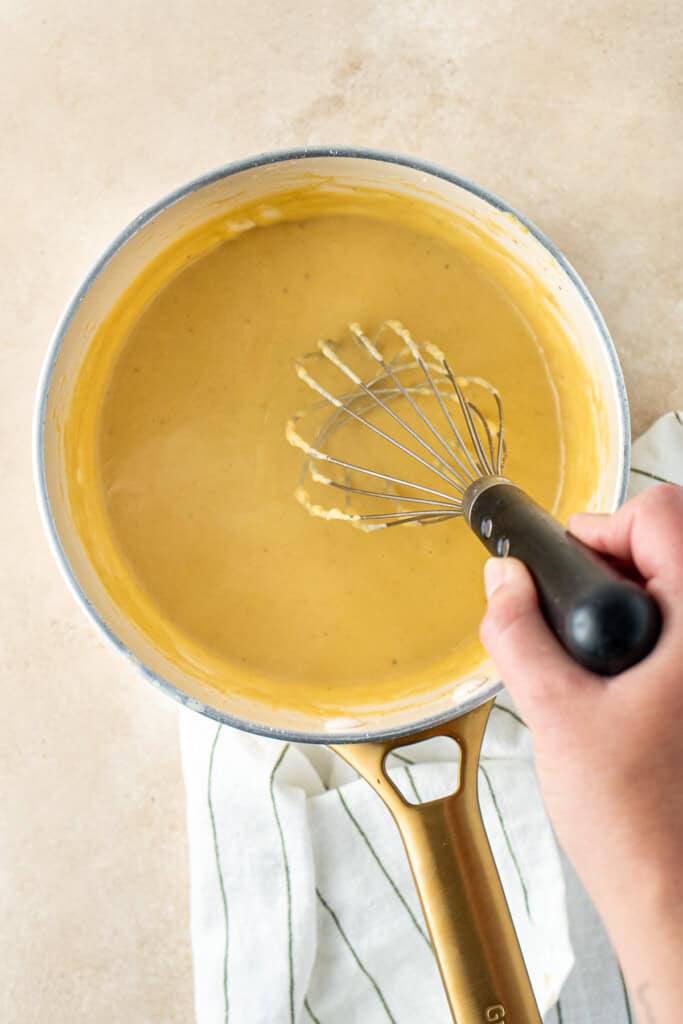 Making the cheesy dairy free béchamel in a saucepan with a whisk.