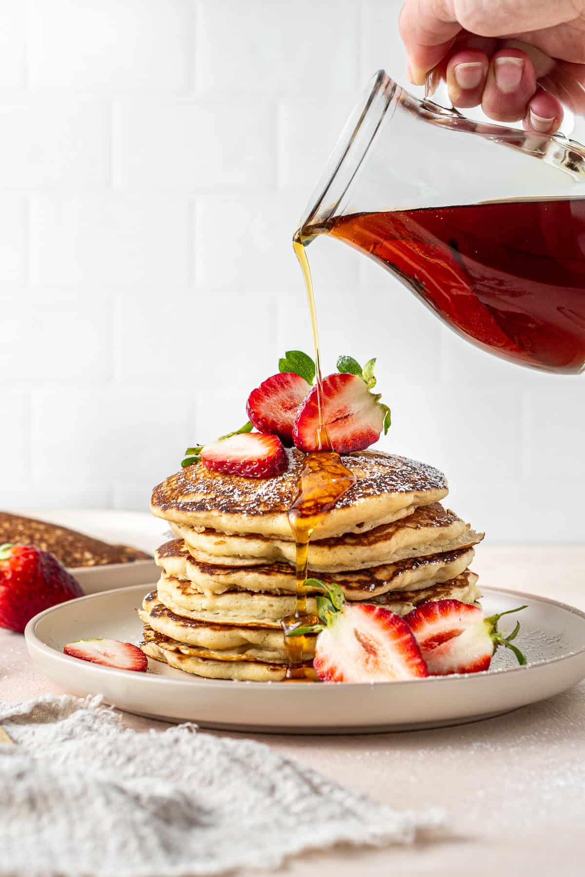 Pouring maple syrup over a stack of dairy free pancakes with strawberries.