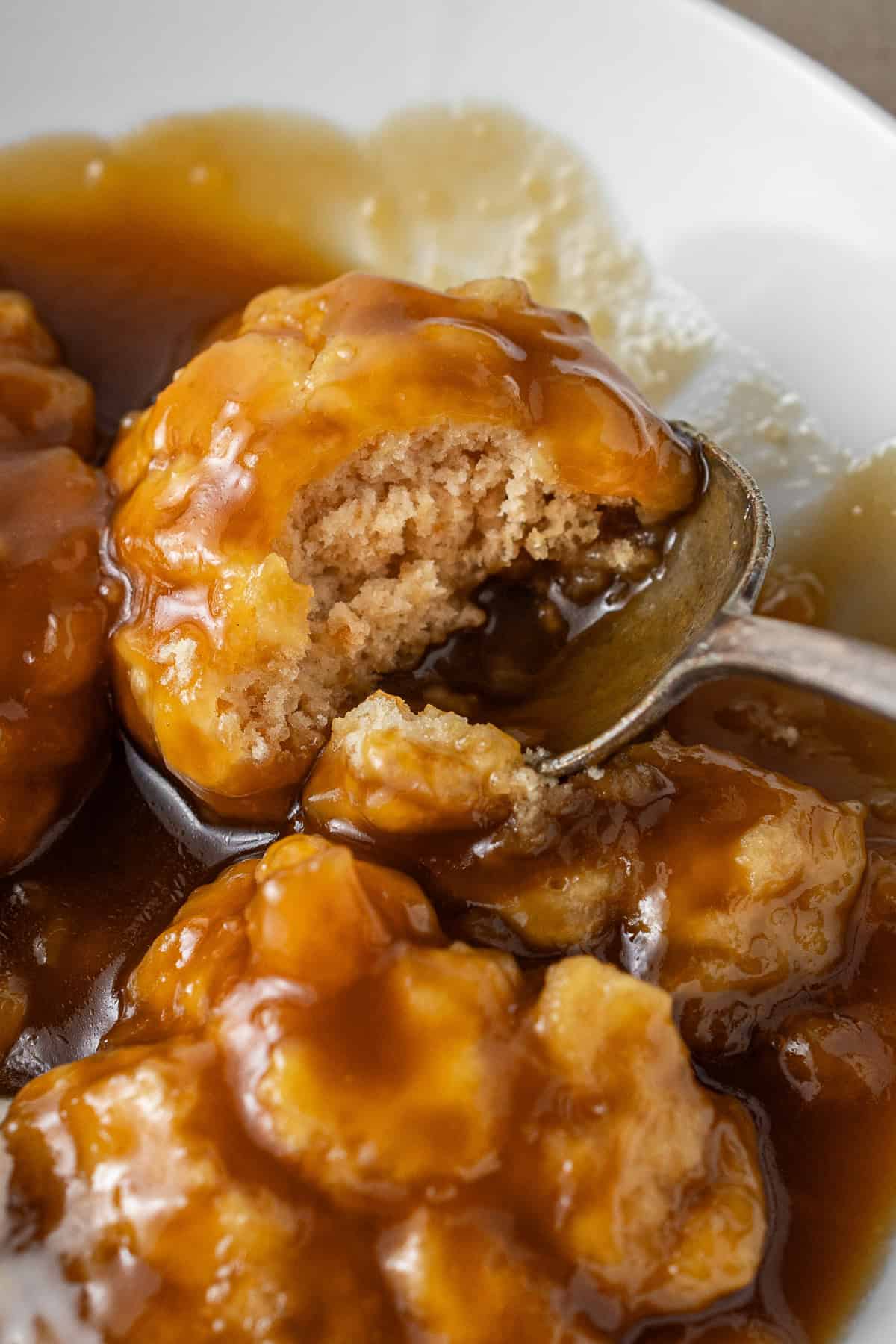 A close up of a dumpling in sauce with a bite taken.