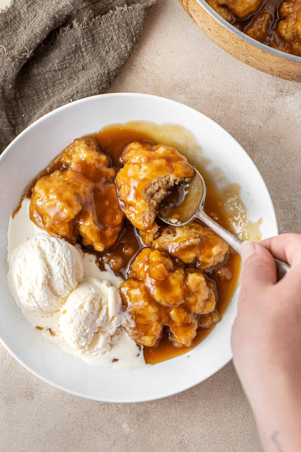 A hand taking a spoonful of golden syrup dumplings served with ice cream.