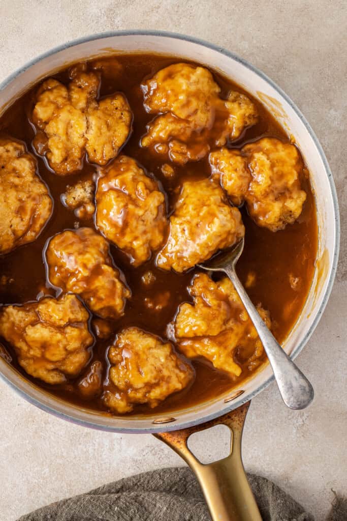 A spoon in the pan of steamed dumplings in the golden syrup sauce.