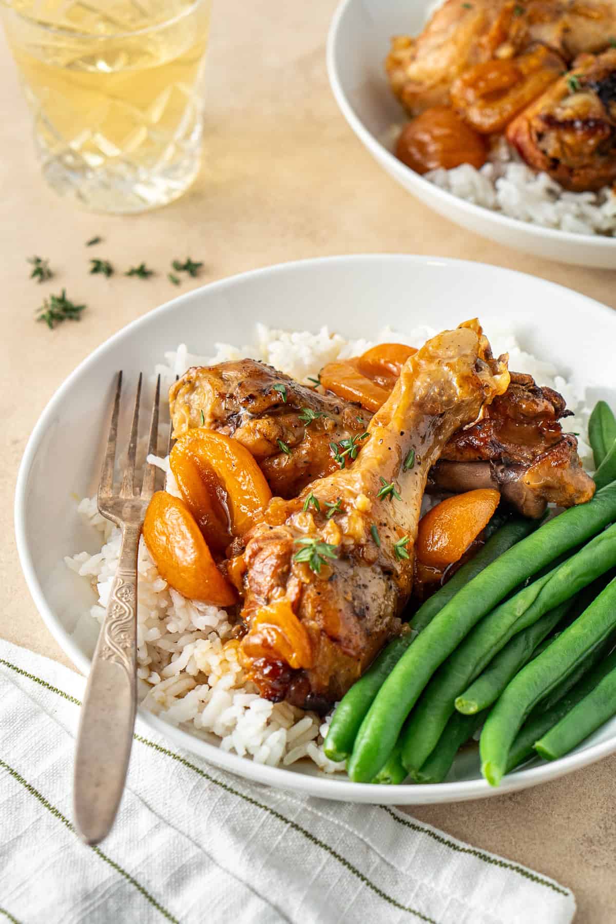 Close up of the apricot chicken drumsticks in a bowl with a fork and a side of vegetables.