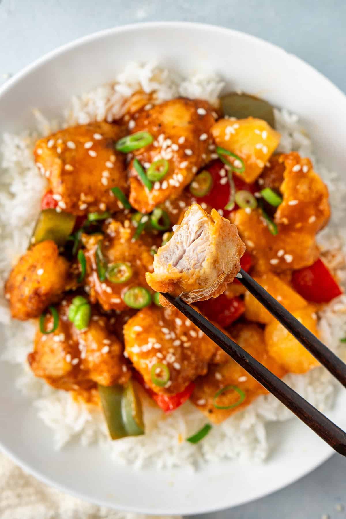 Chopsticks holding a piece of chicken with a bite taken.