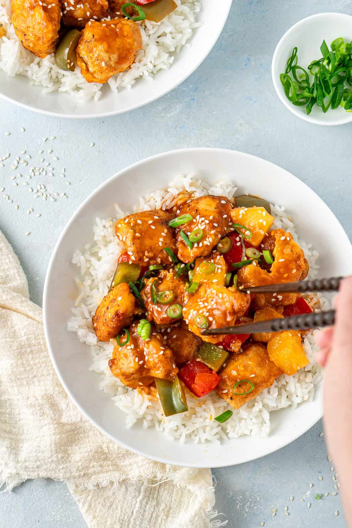 Chopsticks picking up a piece of sweet and sour chicken.