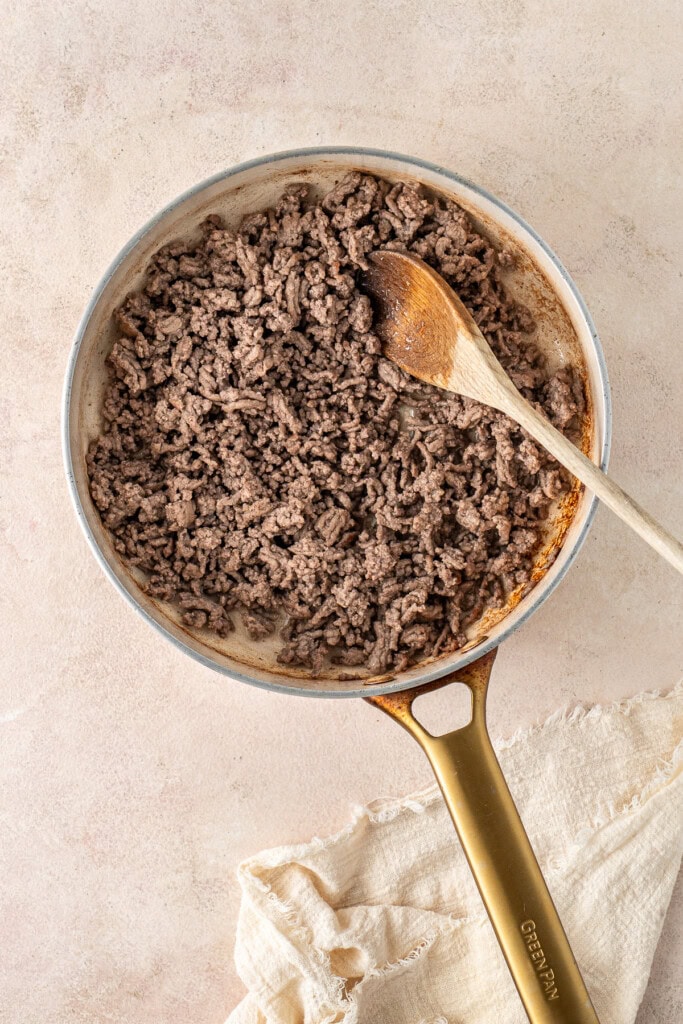 Sautéing the ground beef in a pan with a wooden spoon.
