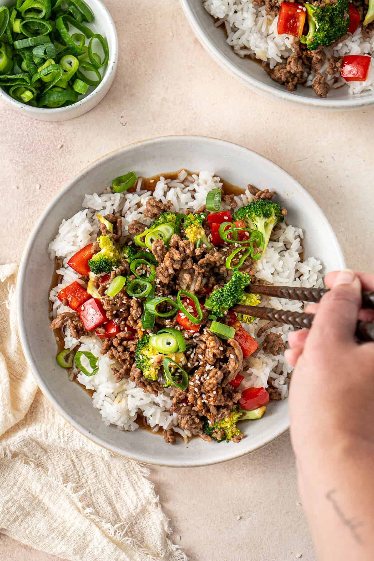 A hand using chopsticks to take a bite of the ground beef teriyaki bowl.