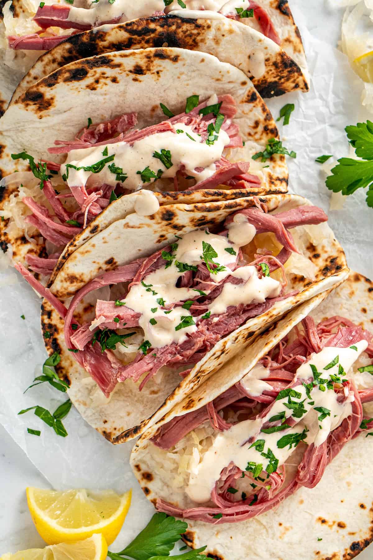 Corned beef tacos with white sauce and parsley.