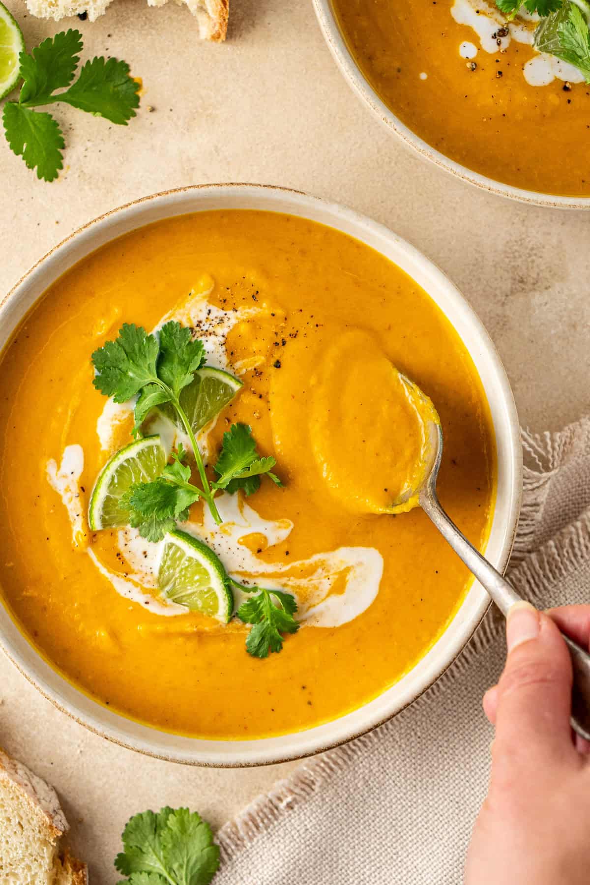 A hand holding a spoon in the creamy orange soup.