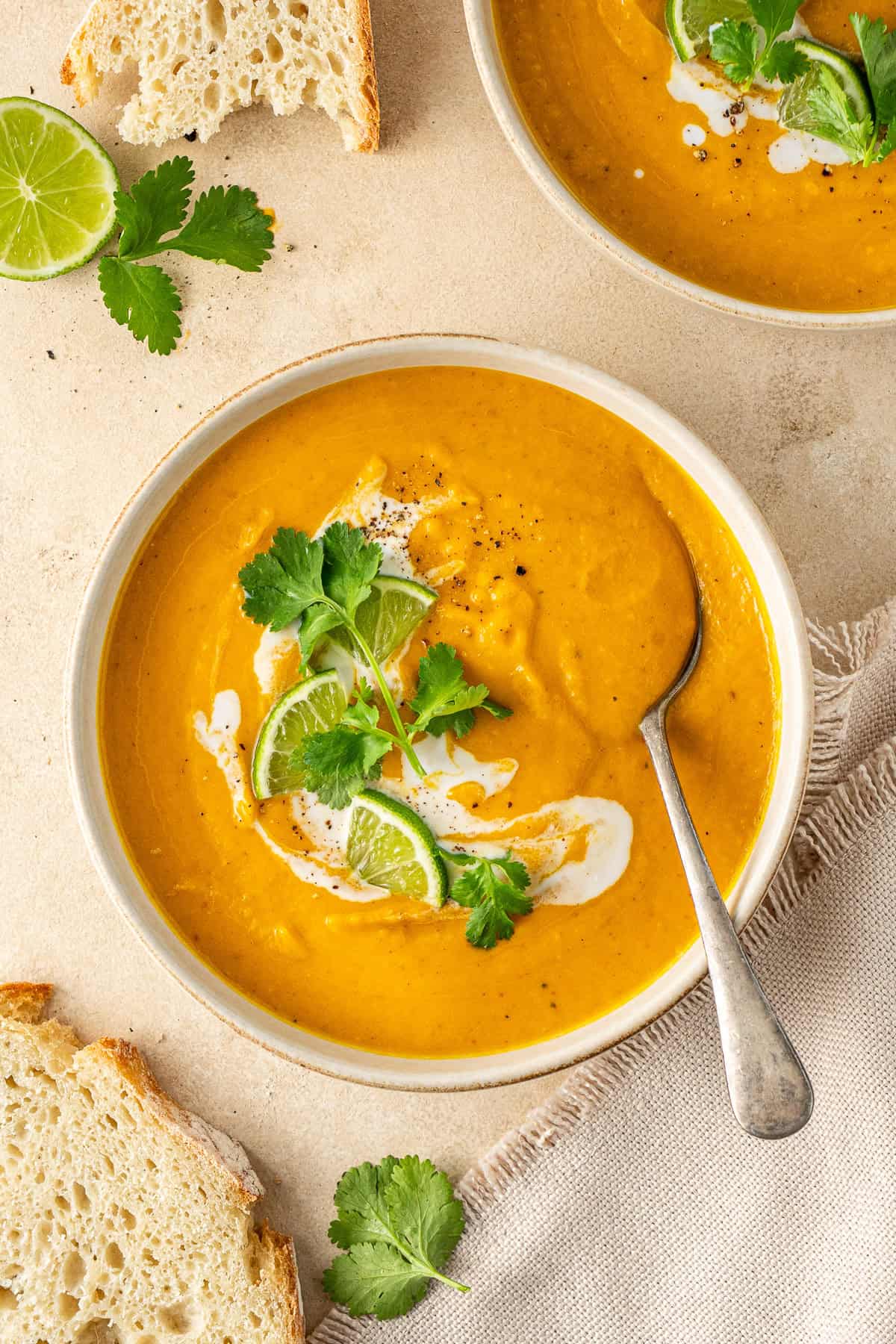 The thai pumpkin soup served into bowls with coriander, lime and a spoon.