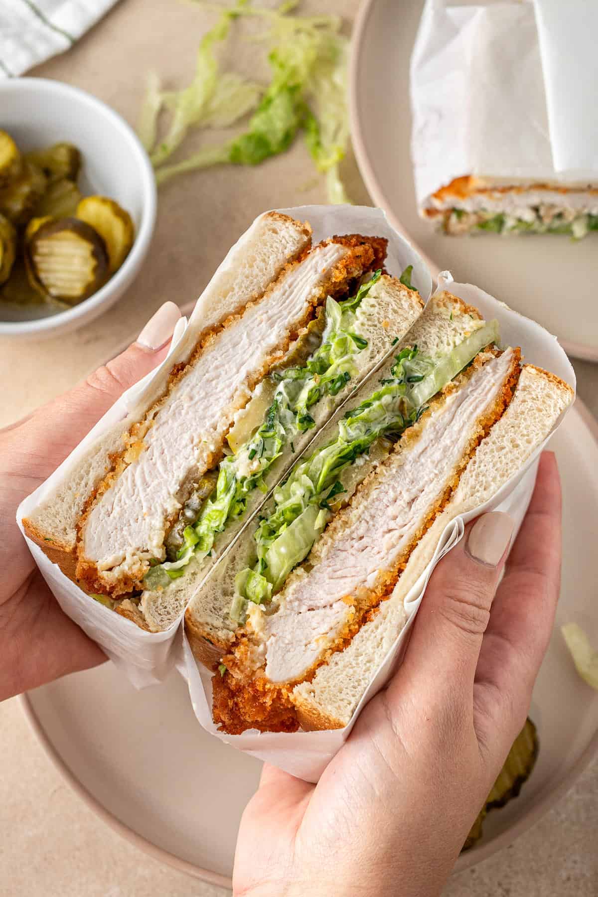 Hands holding a chicken schnitzel sandwich cut in half.