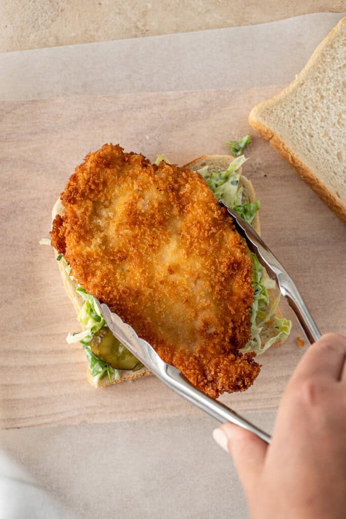 Adding the chicken schnitzel to the sandwich.