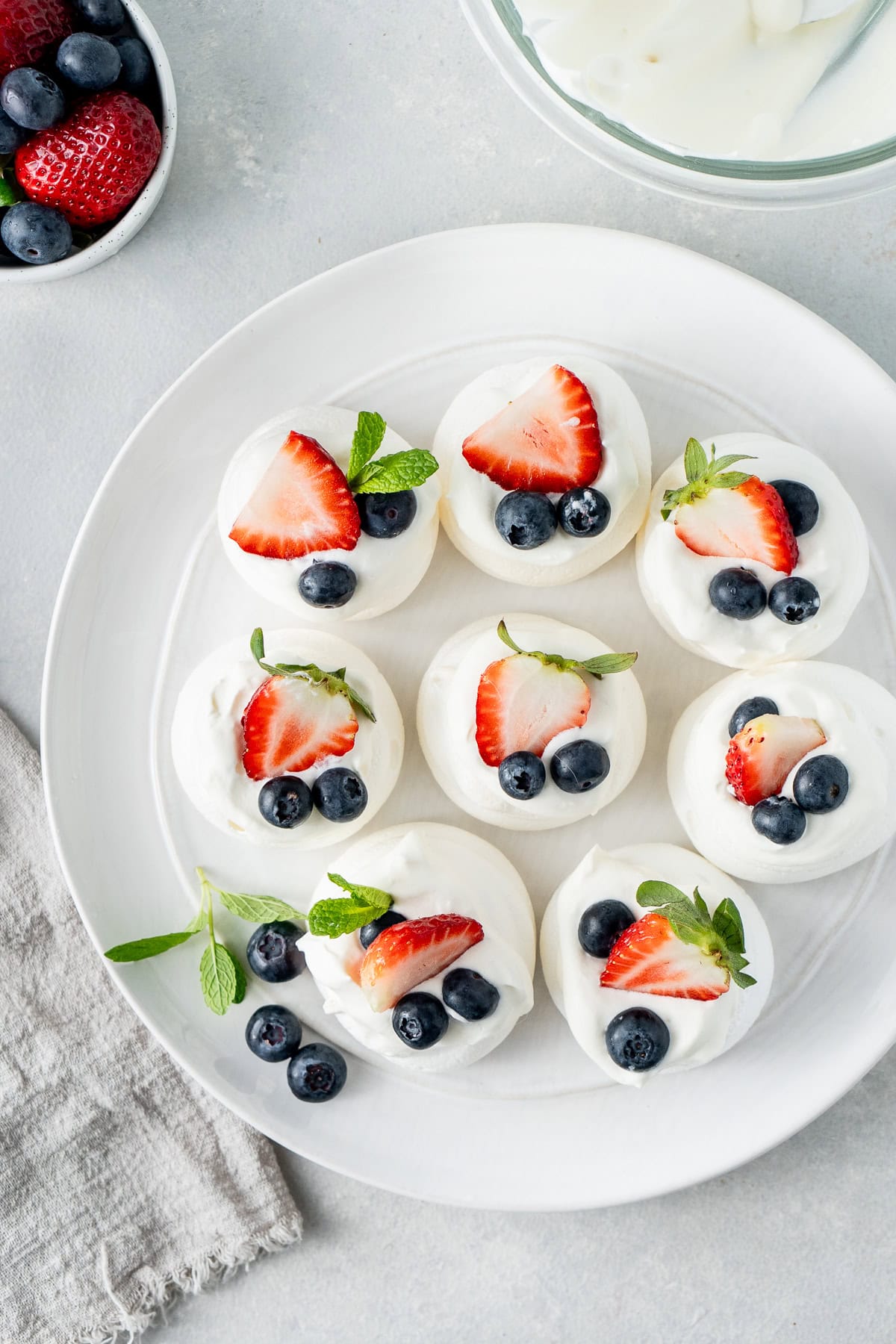 A plate of mini pavlovas with cream and fruit.