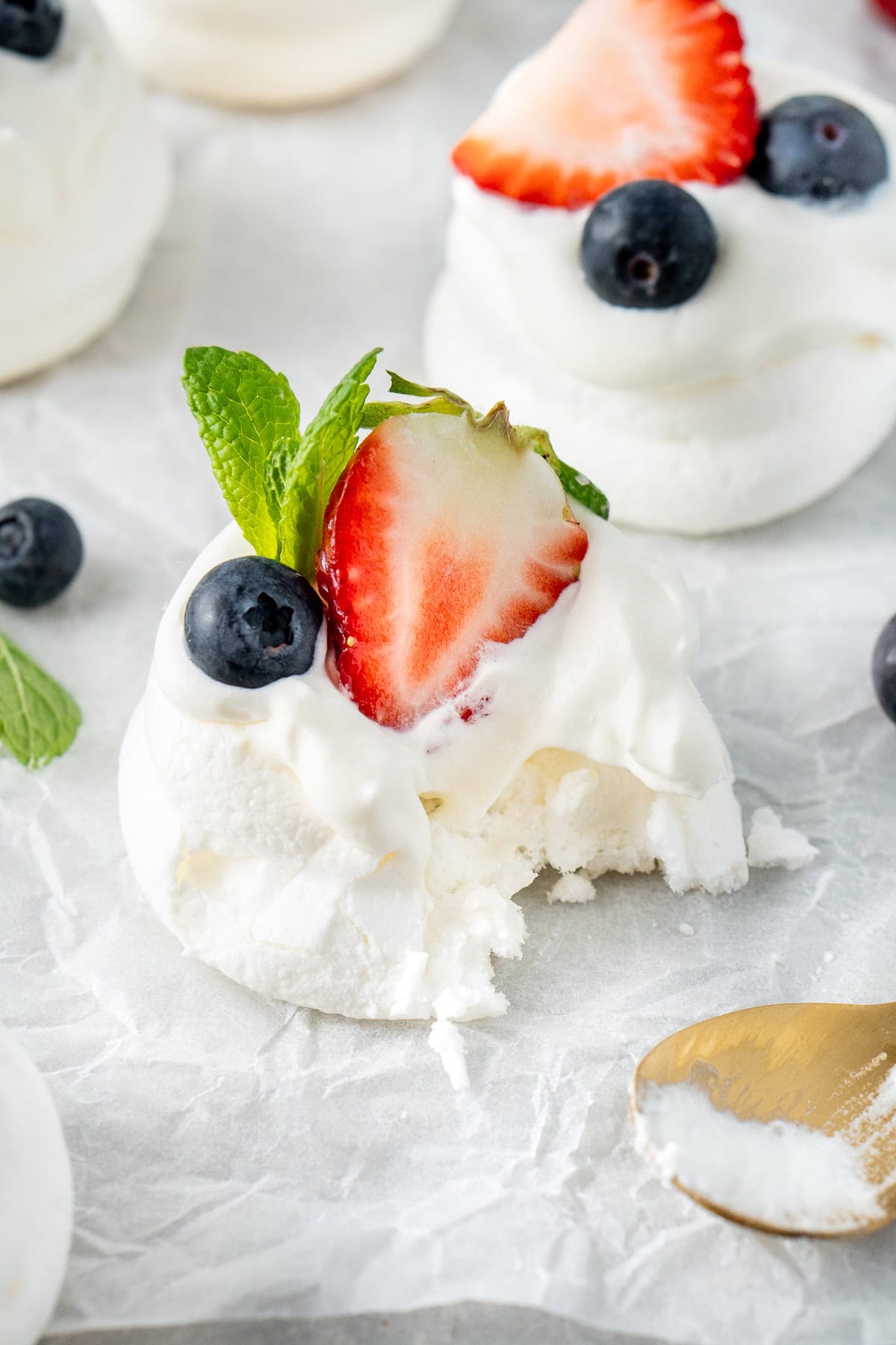 A mini pavlova with cream and fruit and a bite taken.