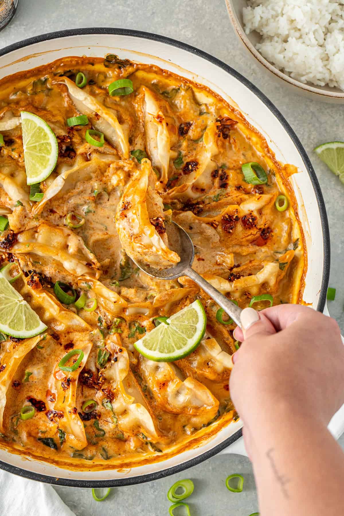 A hand serving out one of the dumplings from the sauce.