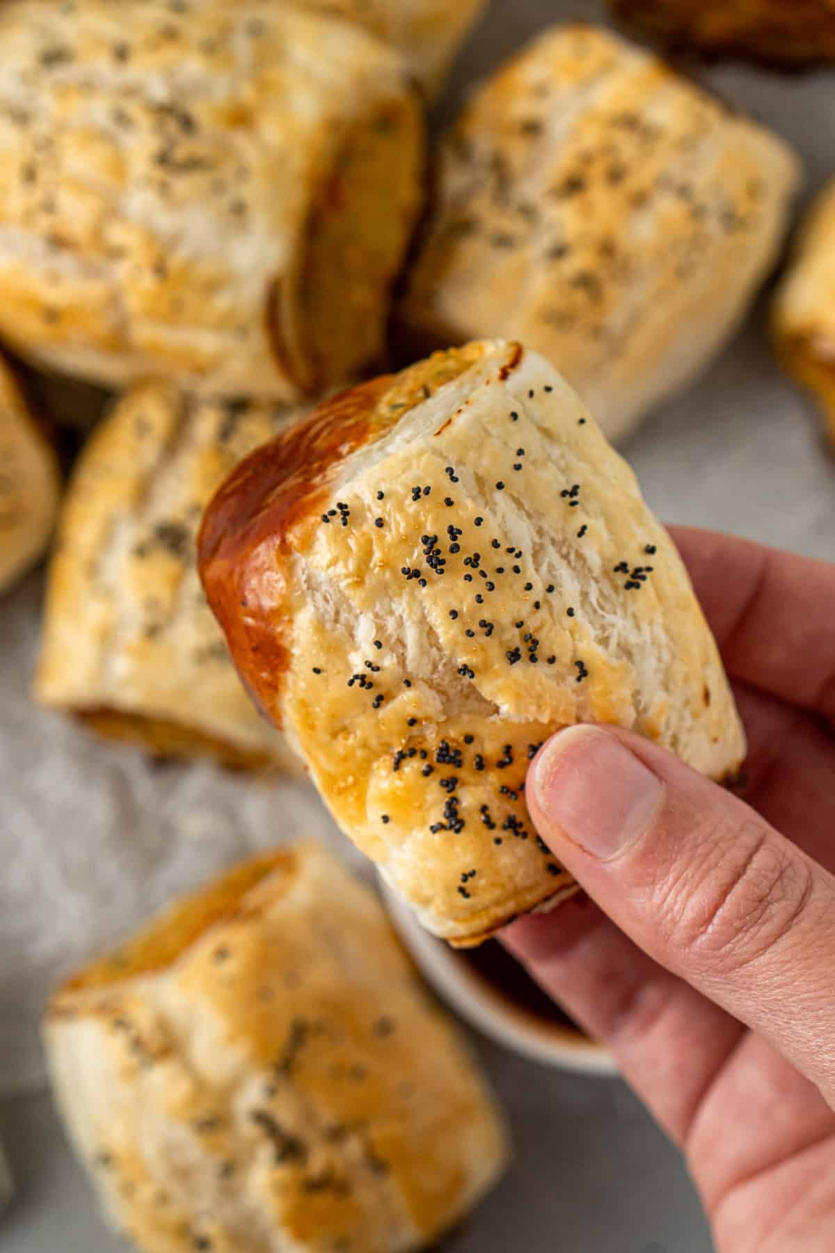 A hand holding a chicken sausage roll dunked in sauce. 