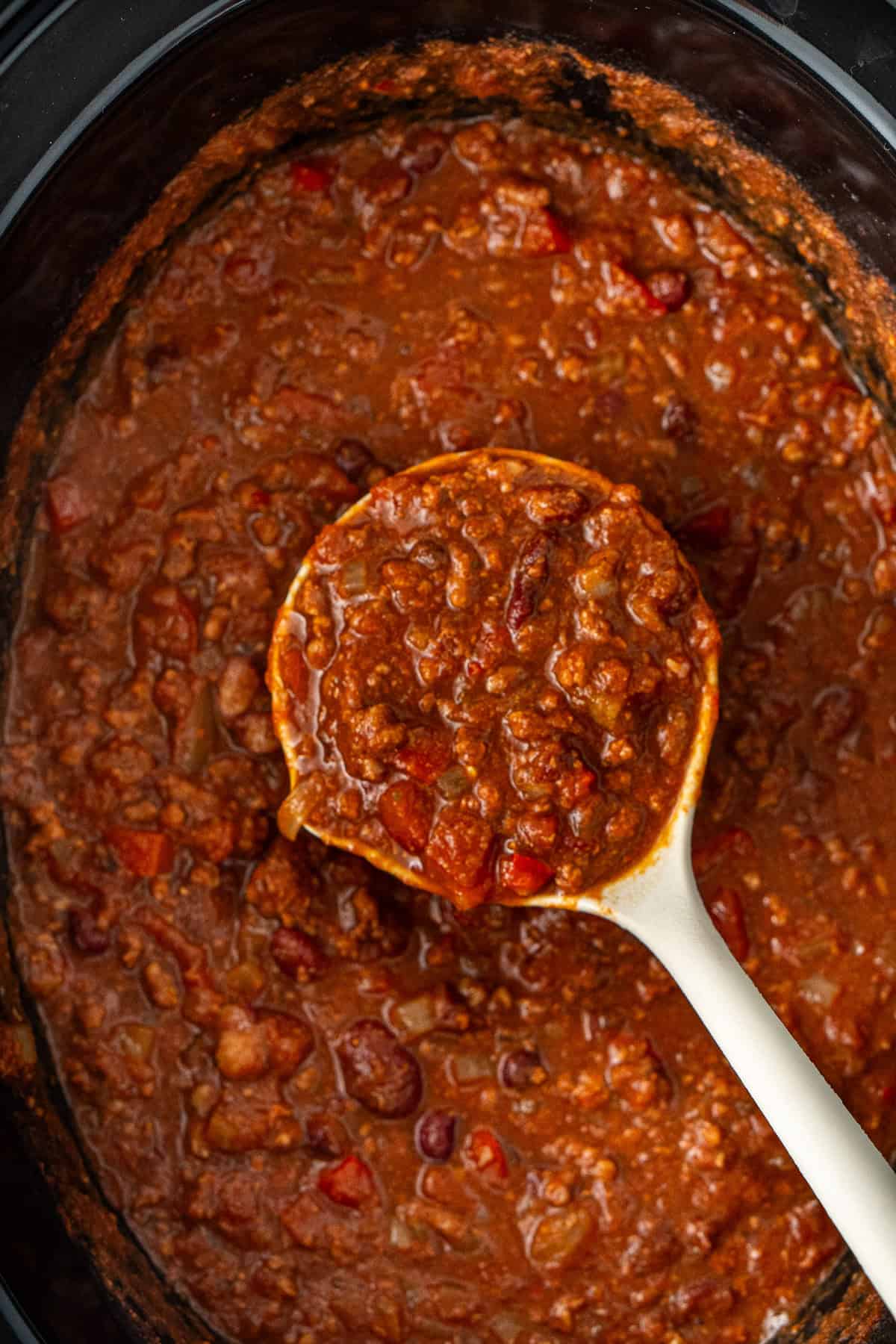 A spoon scooping up the cooked beef chilli from the slow cooker.