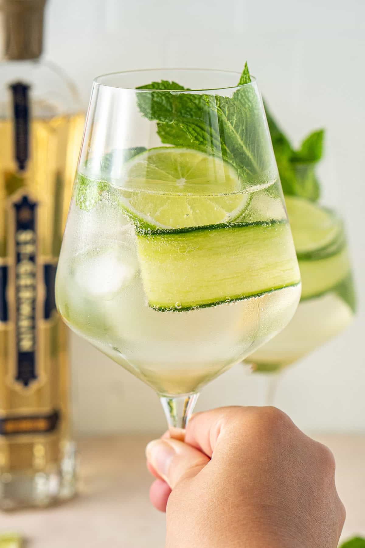 A hand holding up a Hugo spritz cocktail. 