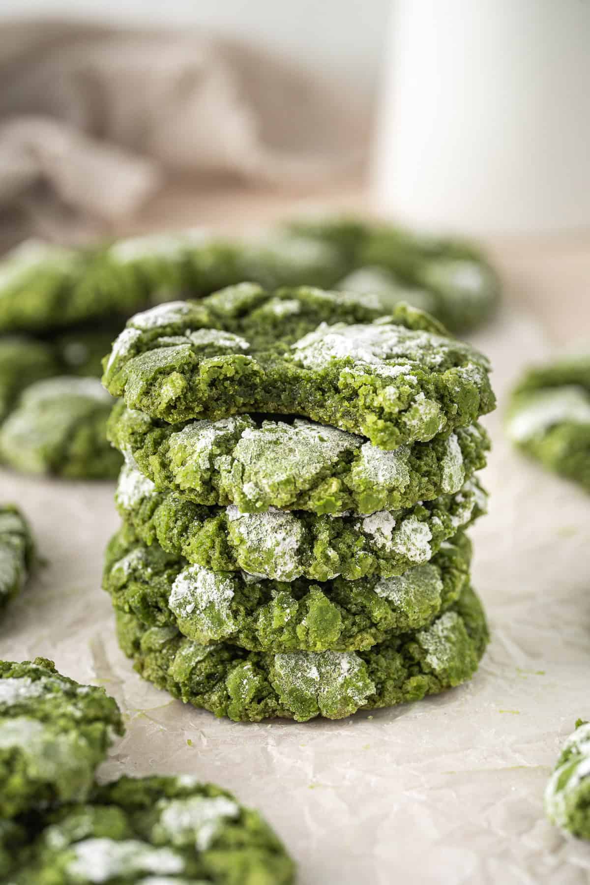 A stack of matcha crinkle cookies, one with a bite taken.