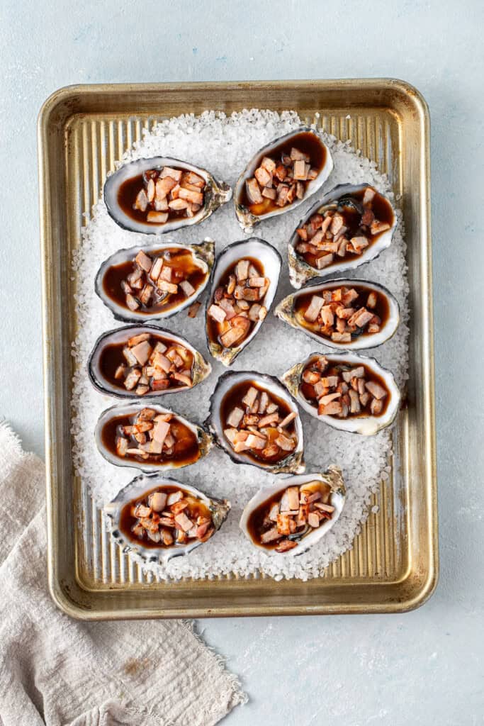 The filled oysters on a bed of rock salt on a baking tray.