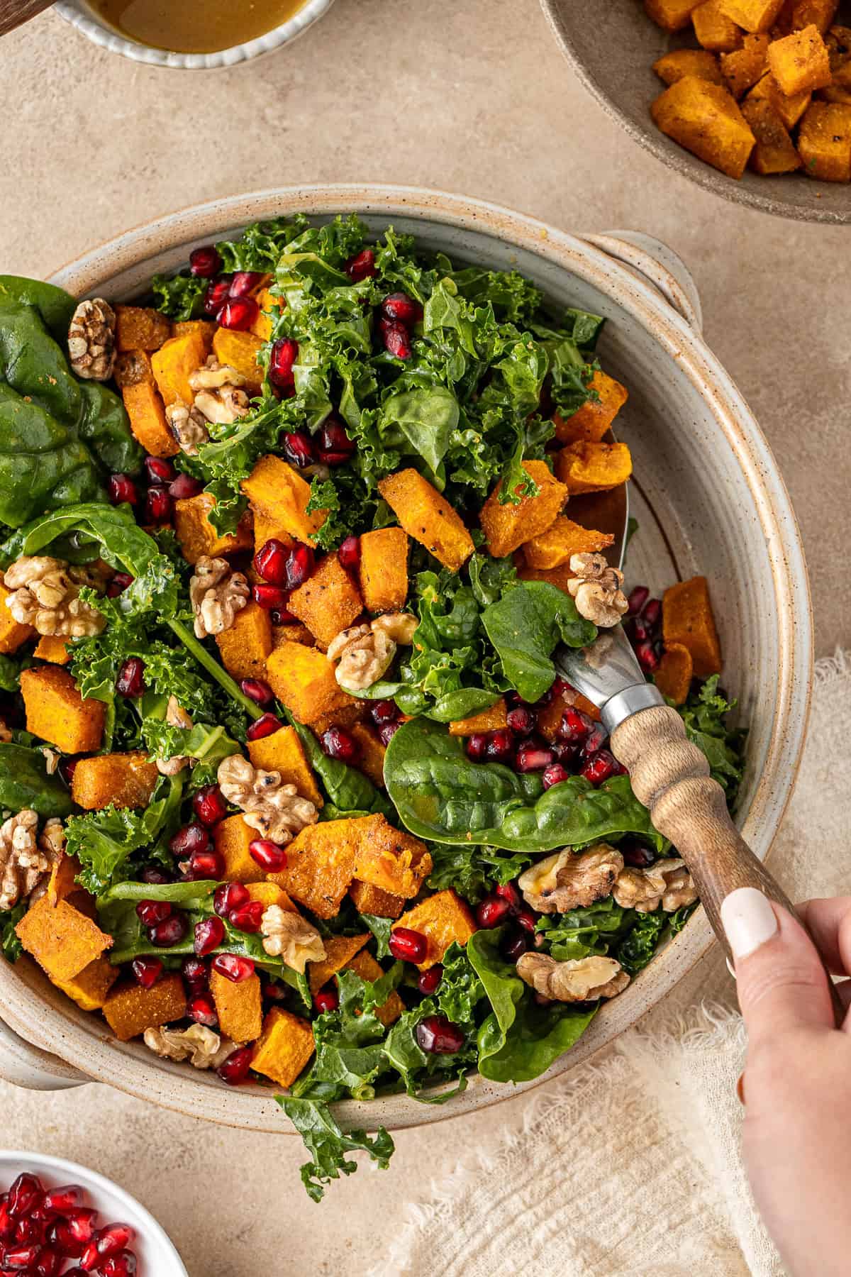 A hand using a large spoon to serve out the roasted pumpkin salad.