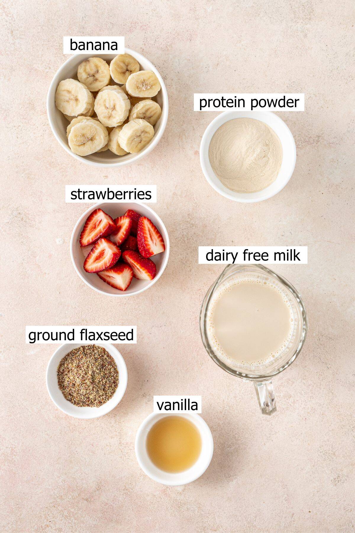 All ingredients needed to make a strawberry banana smoothie laid out in bowls.