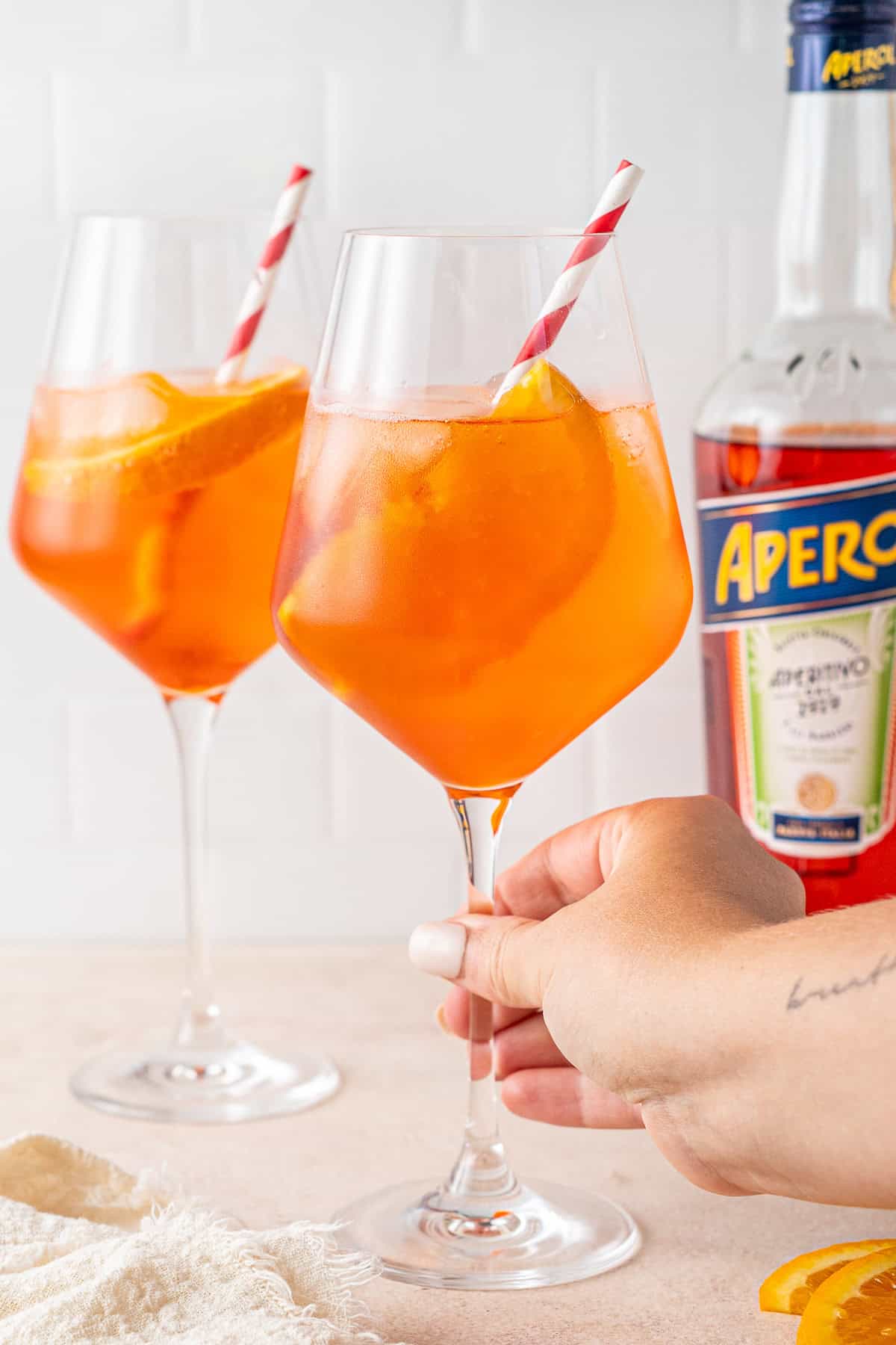 A hand holding the stem of an aperol spritz glass.