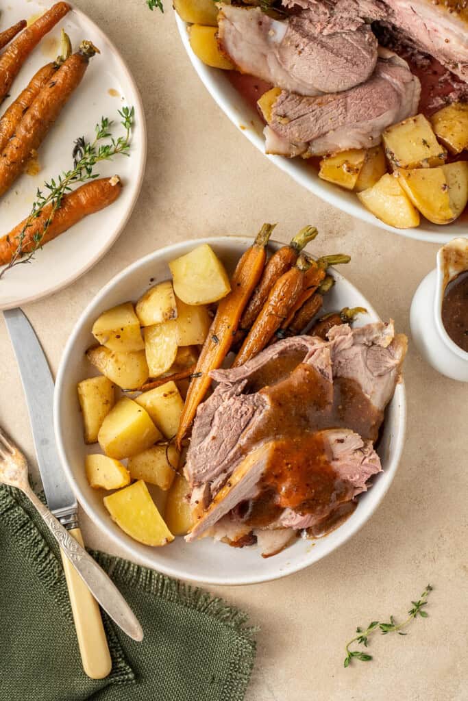 The roast lamb served on a plate with potatoes and carrots.