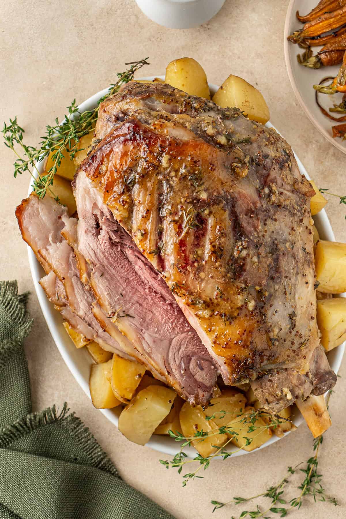 The glazed leg of lamb carved on a plate with potatoes.