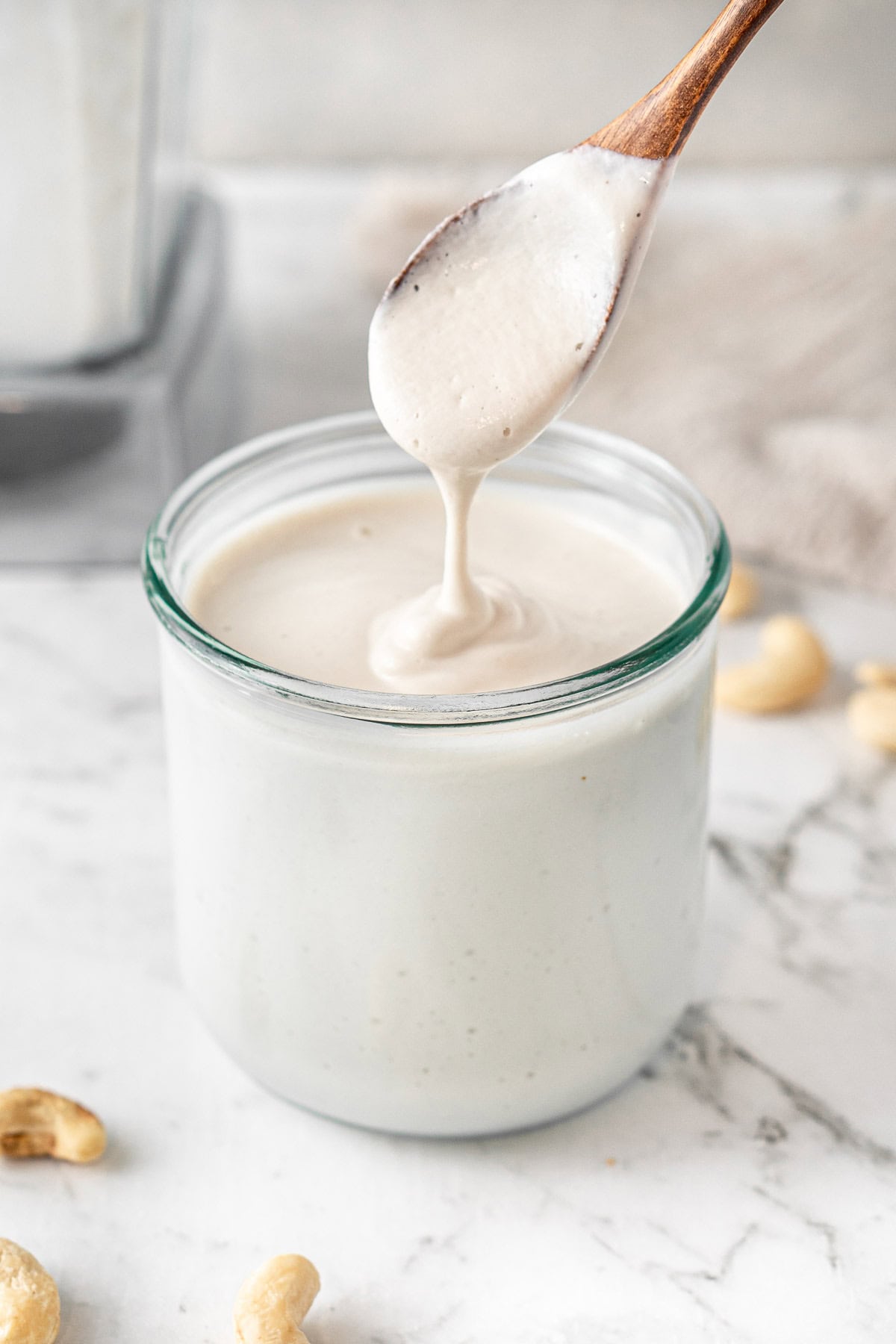 A spoon drizzling the cashew cream in a jar.
