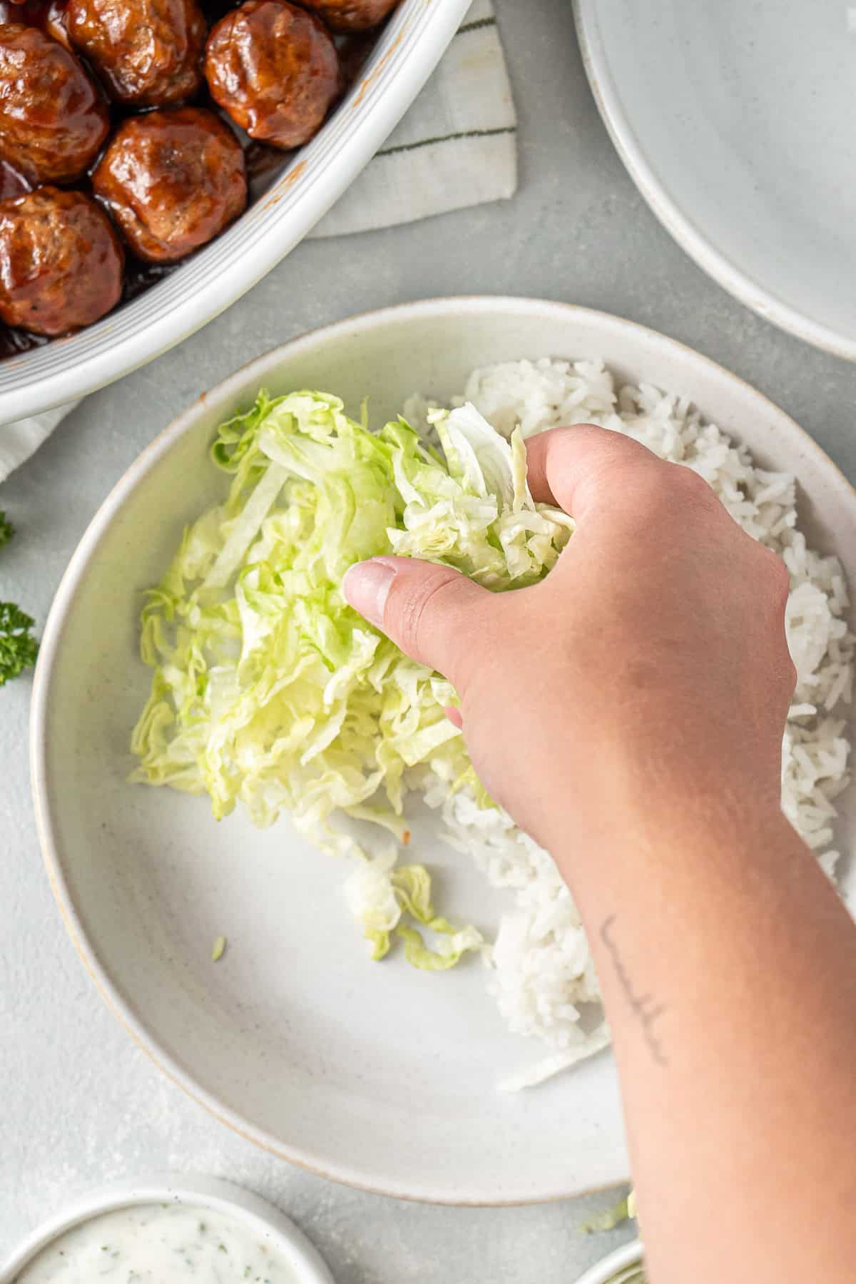 Adding the lettuce to the bowl with rice.