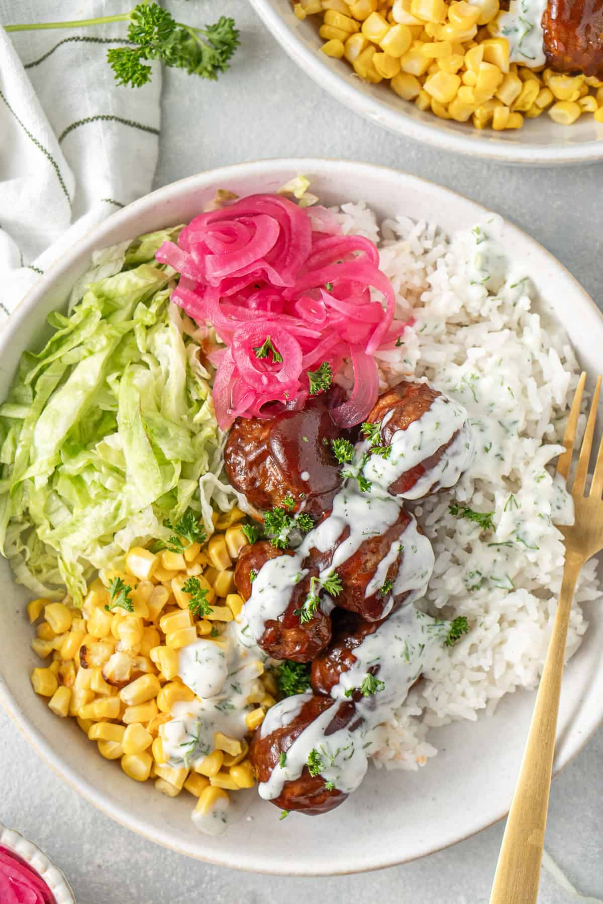 Close up of a rice bowl with bbq meatballs, corn, lettuce and pickled red onions.