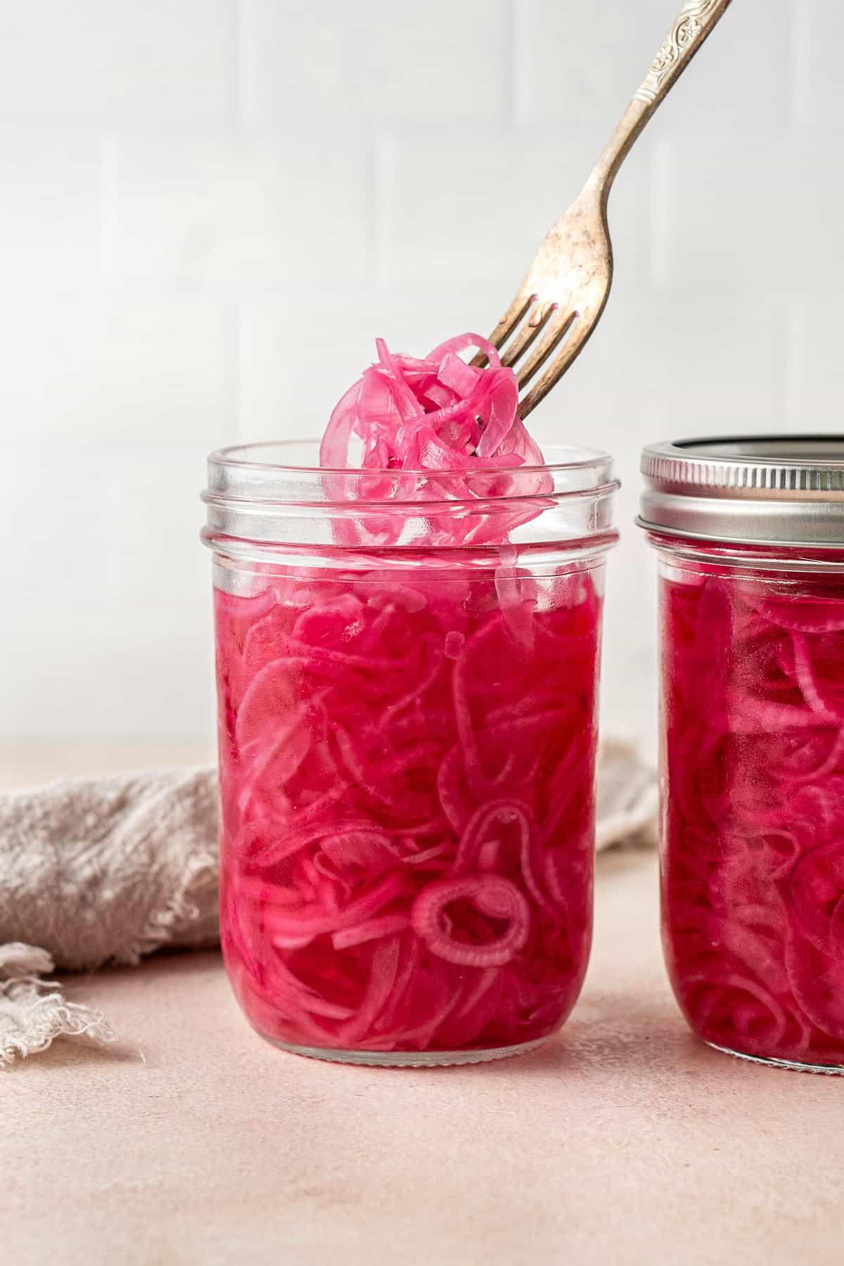 A fork pulling out some of the bright pink pickles onions from a jar.