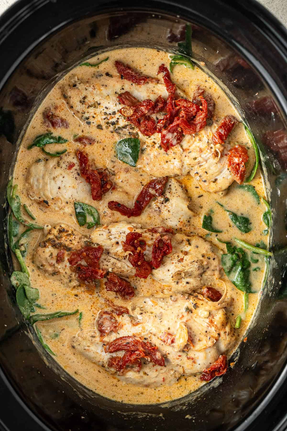 Adding the chicken and spinach to the creamy sauce in the slow cooker.