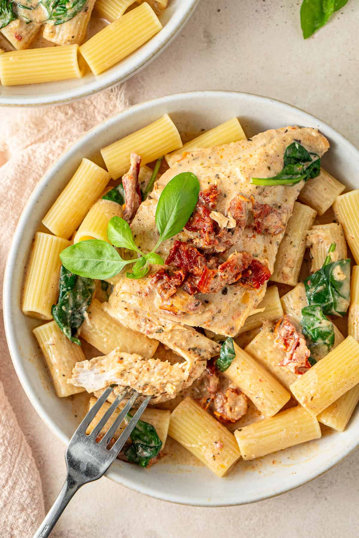 Creamy chicken breast on top of pasta on a white plate.