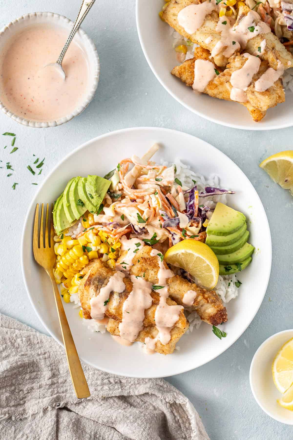 Fish taco bowls with lemon, avocado and sauce in a white bowl on a blue background.