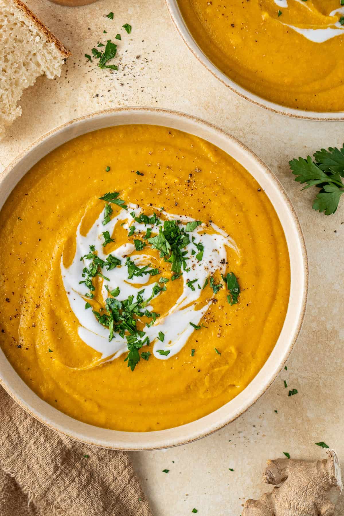 Close up of a bowl of creamy lentil carrot soup with coconut milk and parsley.