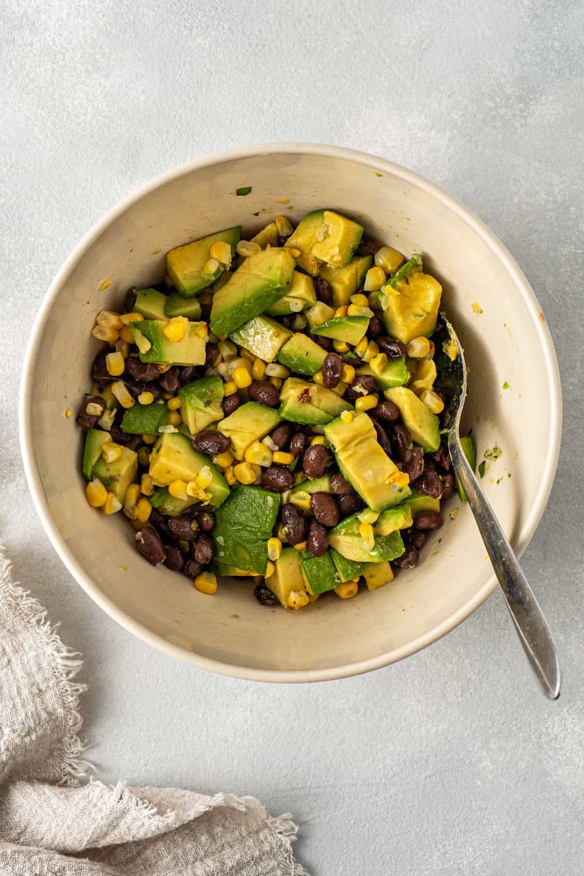 Mixing together the avocado, black beans and corn in a bowl with a spoon.
