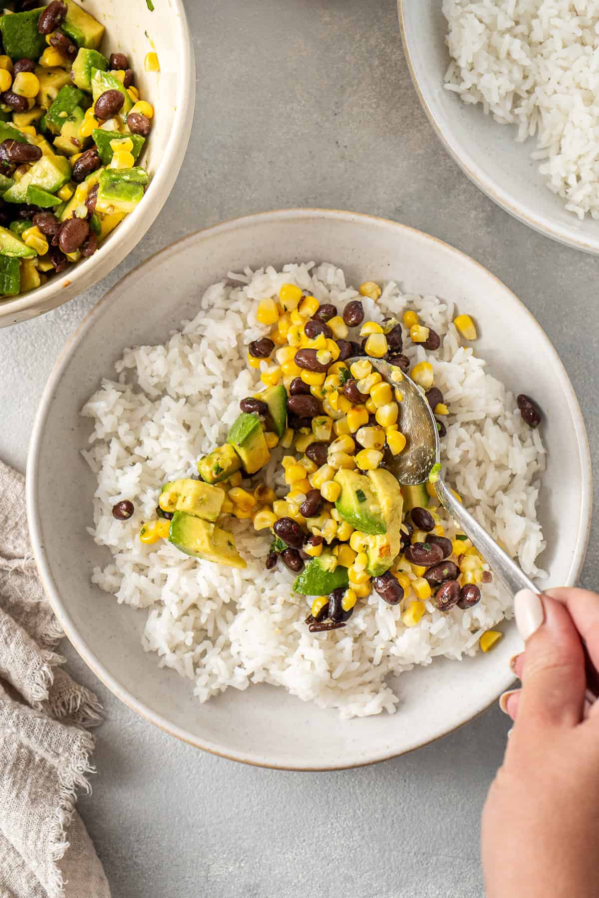 Spooning the black bean, corn and avocado mixture over the rice in white bowls.