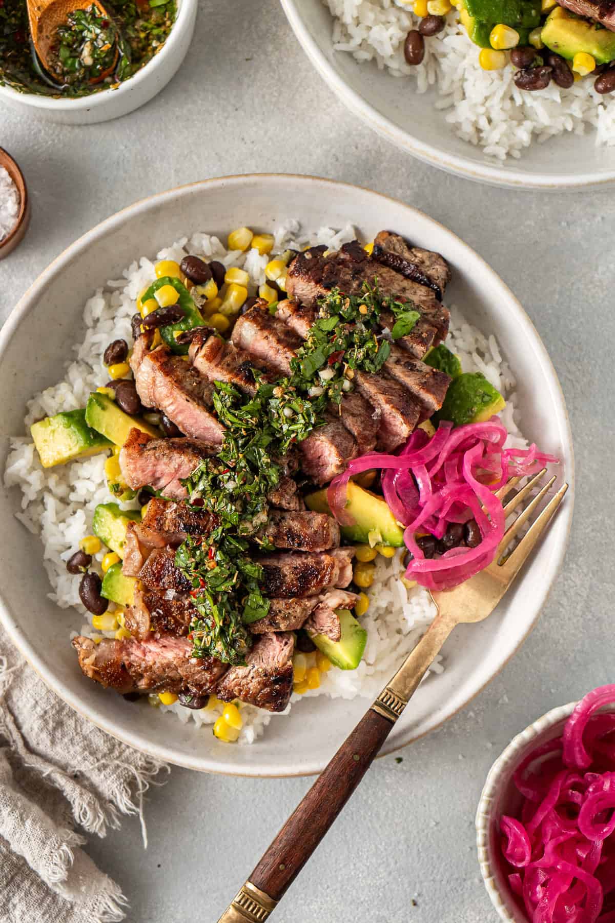 Sliced steak over rice in a white bowl with pickled red onion and a fork.