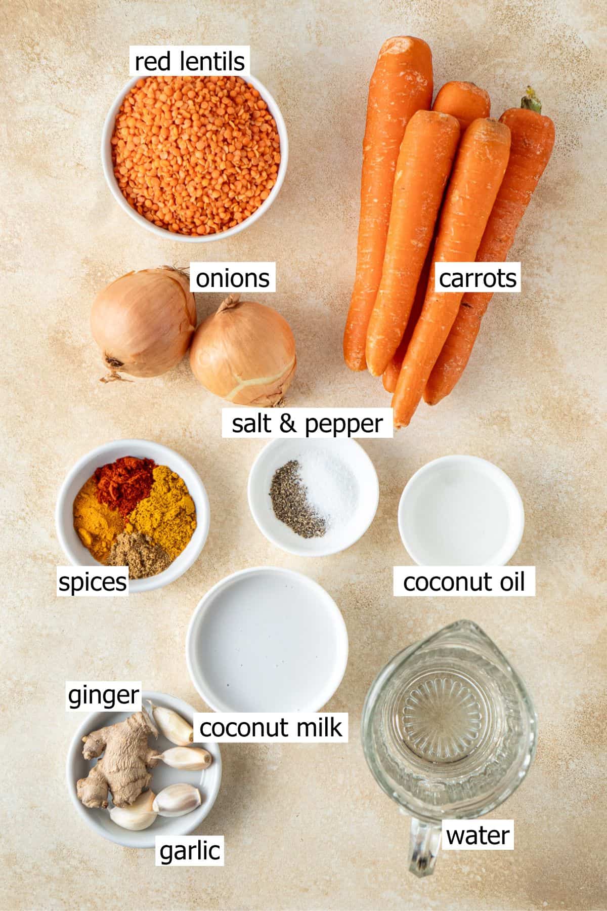 All ingredients needed to make carrot lentil soup laid out in bowls on a brown background.