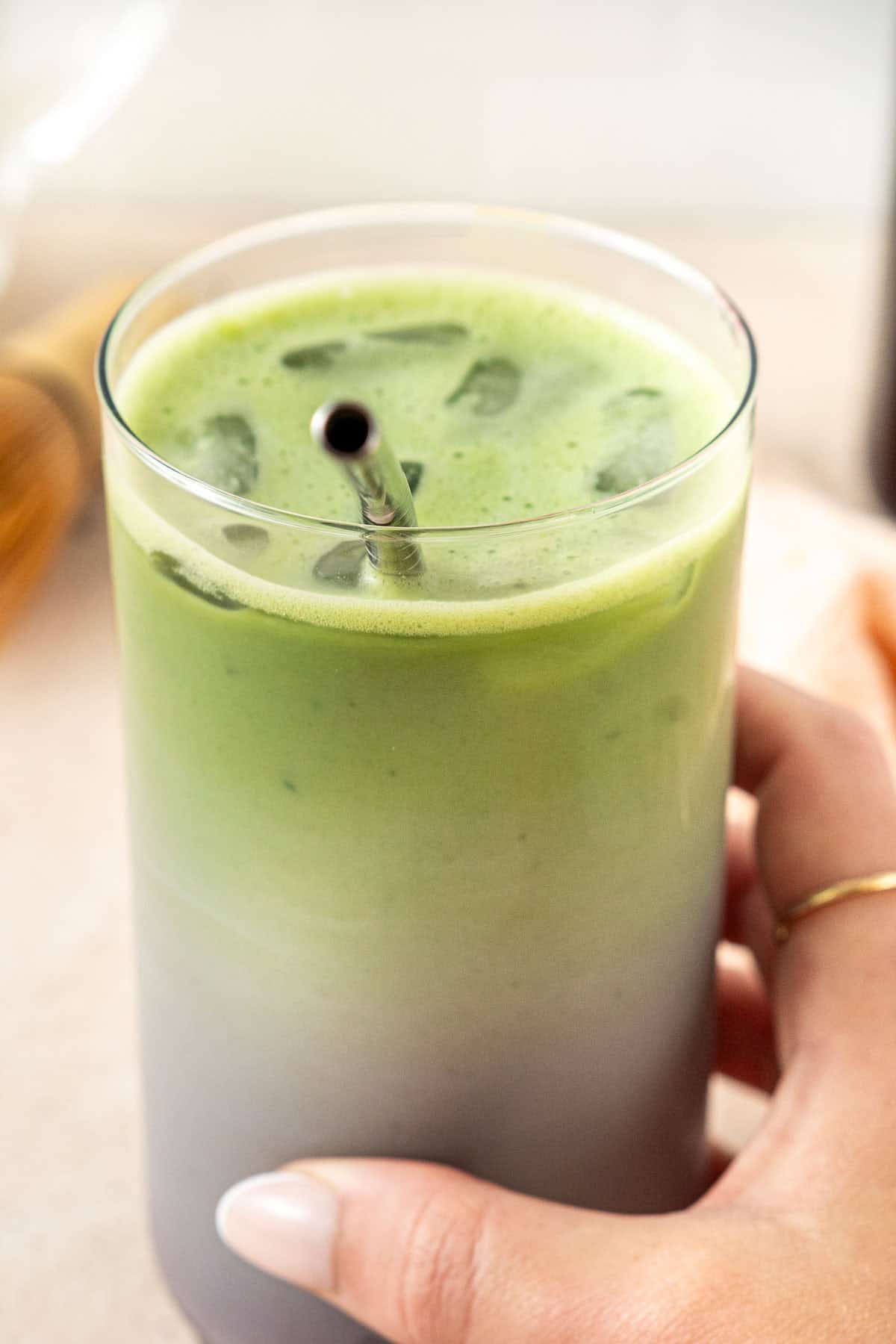 A hand holding the iced blueberry matcha with a straw showing the ombre colour of green to purple. 