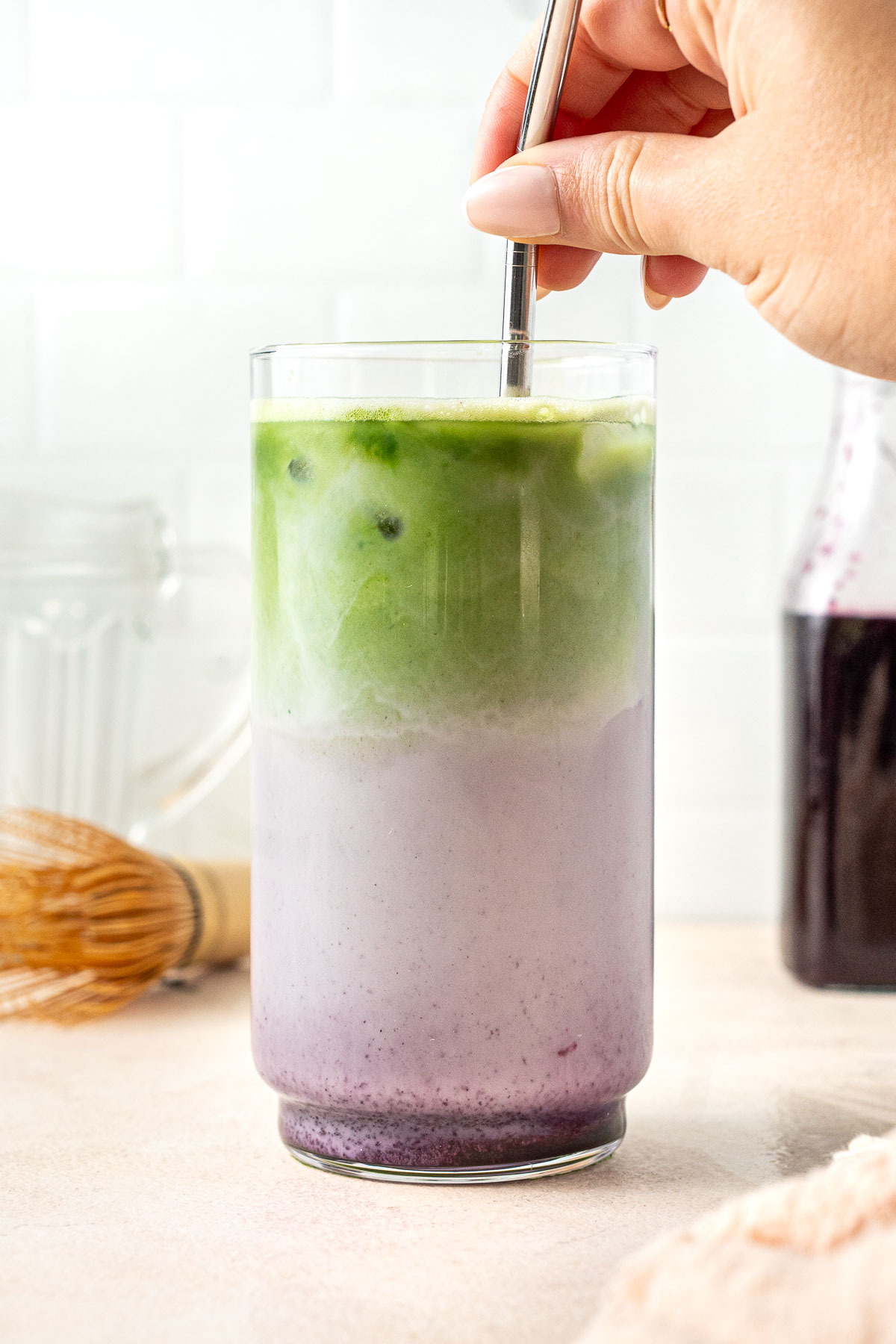 A hand holding a straw mixing up an iced blueberry matcha latte.