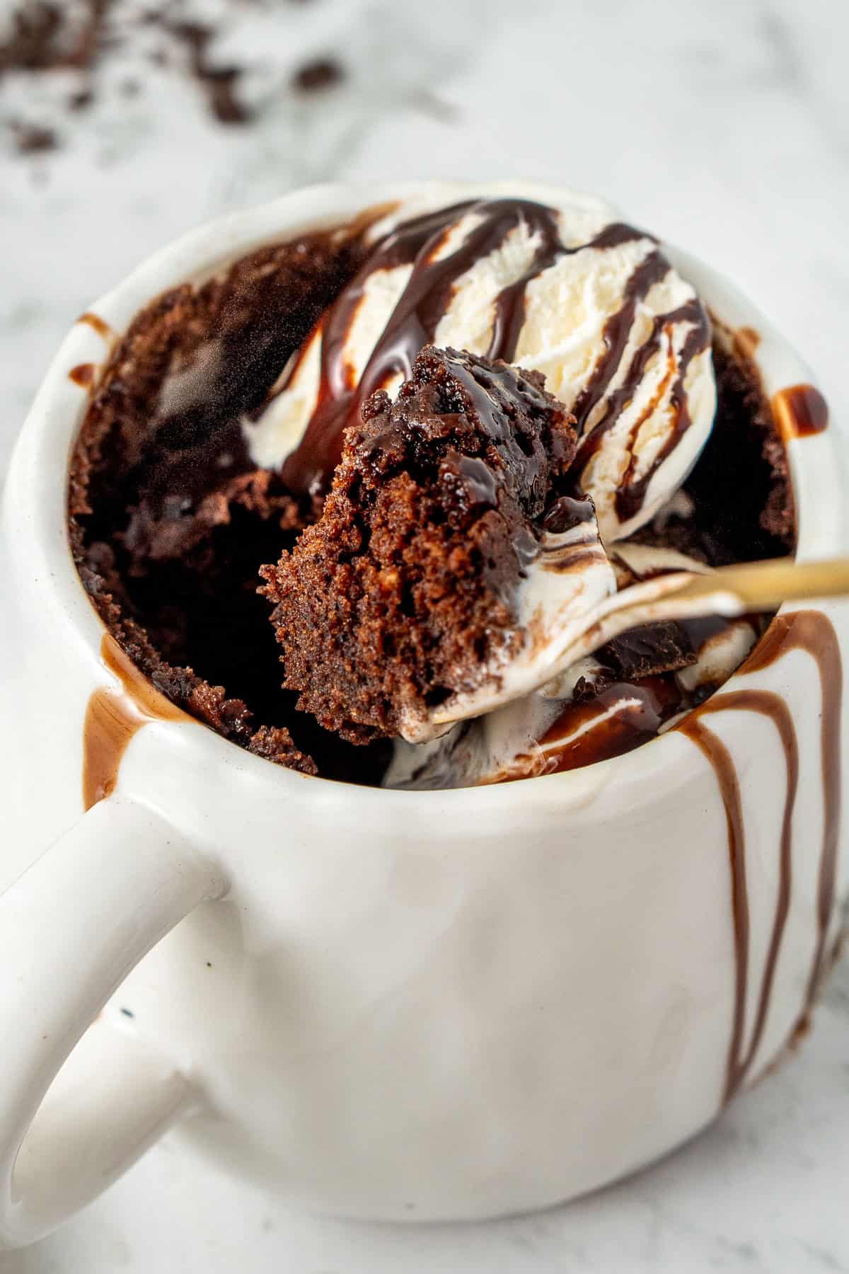 A spoon in a chocolate mug cake with ice cream.
