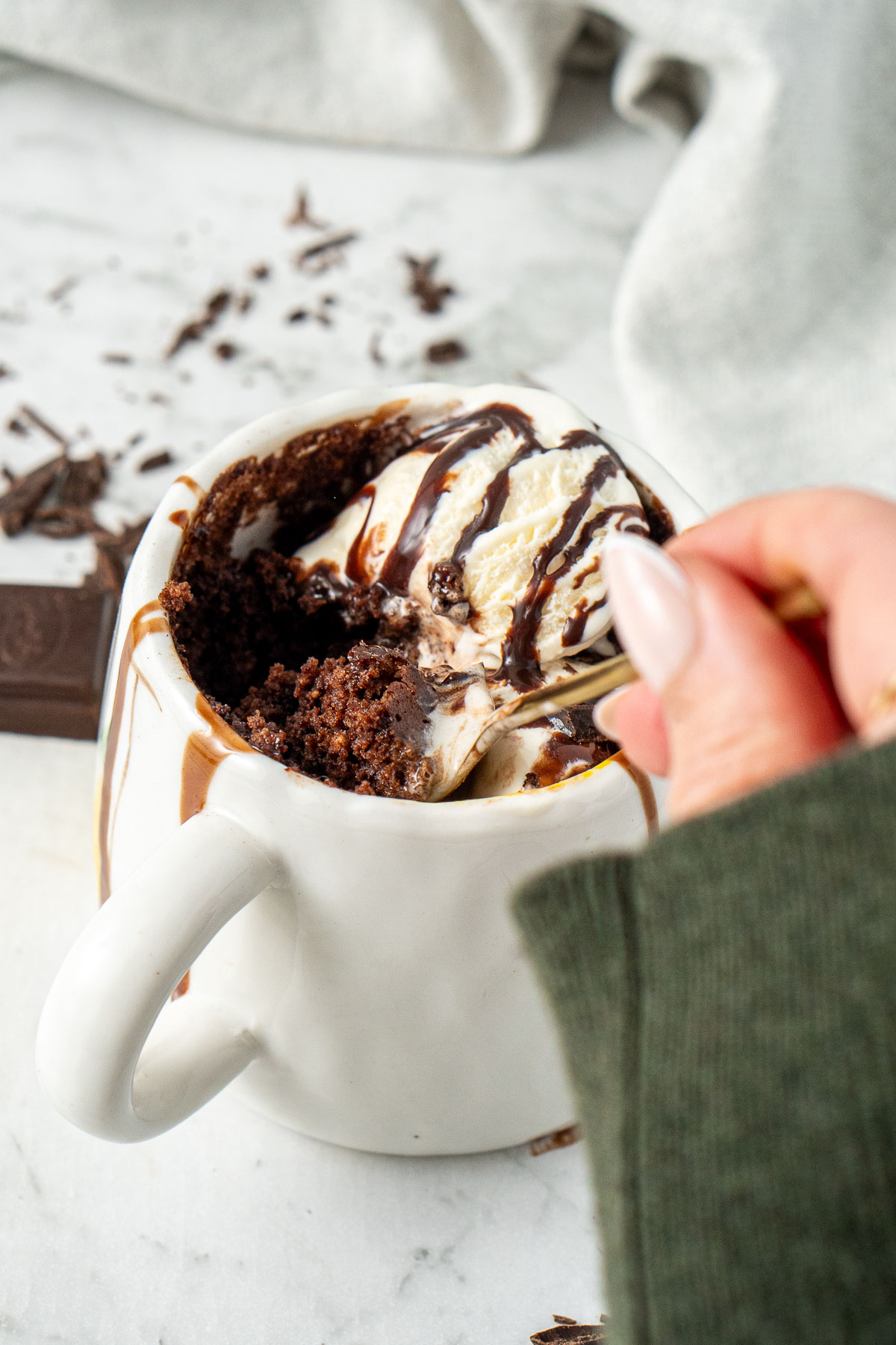 A hand taking a spoonful of dairy free chocolate mug cake with vanilla ice cream.